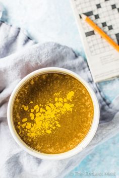 a white bowl filled with yellow liquid next to a crossword puzzle book and pencil