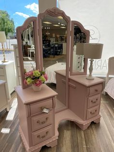 a pink vanity with flowers on it and a mirror in the corner next to it