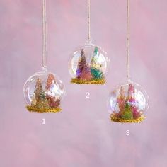 three glass ornaments hanging from strings in front of a pink background with glitter castle silhouettes