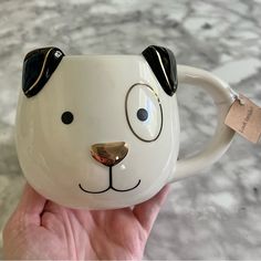 a hand holding a white coffee mug with a dog face on it