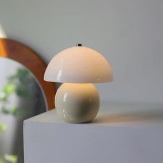 a white table lamp sitting on top of a white block next to a mirror and plant