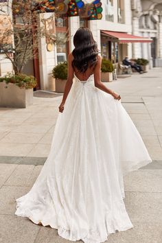 a woman in a wedding dress walking down the street with her back to the camera