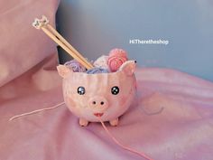 a pink piggy bank with yarn and knitting needles in it's mouth on a pink sheet