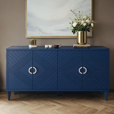 a blue sideboard with gold handles and flowers on top in front of a painting