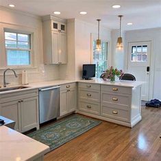 a kitchen with wooden floors and white cabinets, silver appliances and an area rug on the floor