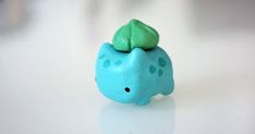 a small blue elephant figurine with a green leaf on its head sitting on a white surface