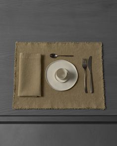 a place setting with silverware and napkins on a linen placemat, next to a knife and fork