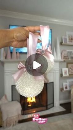 a person is holding some balls in front of a fire place with a pink ribbon on it