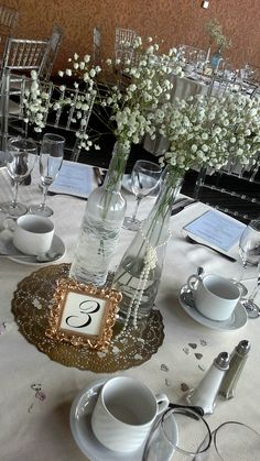 the table is set with white flowers in vases and silver place settings for two people