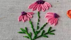 some pink flowers and an orange heart on a gray table cloth with stitches in the shape of hearts