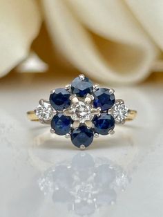 a blue and white diamond ring sitting on top of a table next to a flower