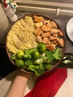 a bowl filled with broccoli and chicken next to a person's hand