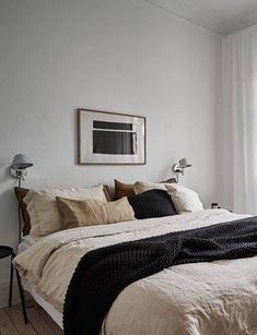 a bed sitting in a bedroom next to a window covered in white sheets and pillows