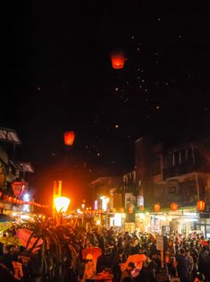 many people are standing in the street at night with lanterns flying overhead and onlookers watching