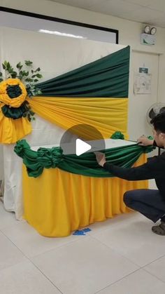 a man kneeling down next to a table covered in green and yellow cloths with flowers on it