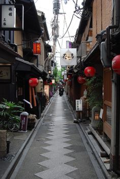 an alley way with buildings and signs on both sides, surrounded by greenery in the background