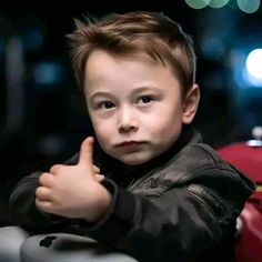 a little boy giving the thumbs up sign in front of his face with blurry lights behind him