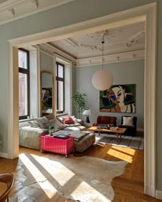 a living room filled with lots of furniture next to tall windows on top of a hard wood floor