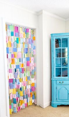 a blue china cabinet sitting next to a wall covered in post it notes and a colorful curtain