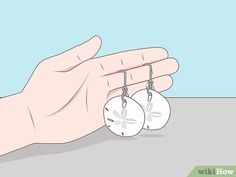 a hand holding two small white earrings with sand dollar charms hanging from it's sides