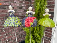 three colorful vases sitting on top of metal rods next to a brick wall and green plant