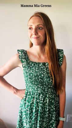 a woman standing with her hands on her hips wearing a green dress and smiling at the camera