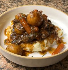 a bowl filled with meat and potatoes covered in gravy on top of a table