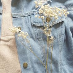 a denim jacket with flowers on the back and button holes in the front, sitting next to a pair of jeans