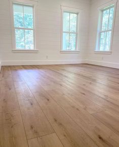 an empty room with three windows and hard wood flooring on one side, white painted walls in the background