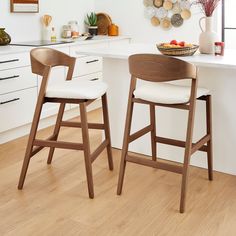 two wooden stools sitting in front of a white counter top next to a bowl of fruit