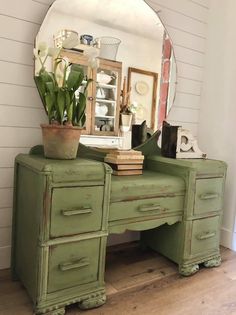 a green dresser with a potted plant on top and a round mirror above it