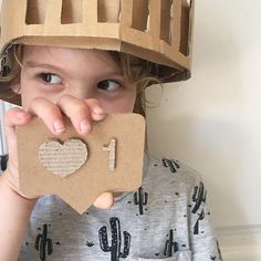 a young child wearing a cardboard crown and holding up a piece of cardboard to his face