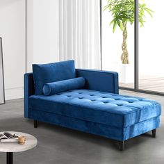 a blue couch sitting in front of a window next to a table with a phone on it