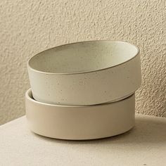 three white bowls stacked on top of each other in front of a beige wall,