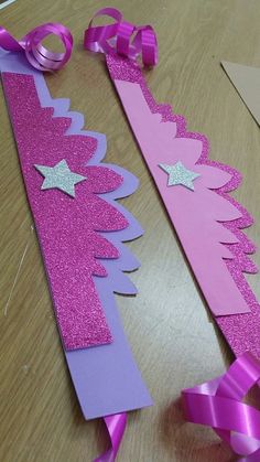 two pink and purple paper christmas trees on a wooden table with ribbon around the edges