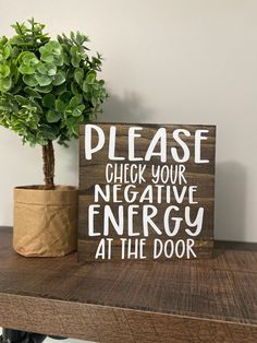 a wooden sign that says please check your negative energy at the door next to a potted plant