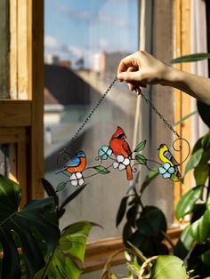 a hand holding a stained glass bird hanging from a chain in front of a window