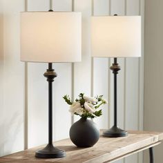 three lamps sitting on top of a wooden table next to a vase with flowers in it