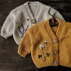 two knitted sweaters sitting on top of a wooden table