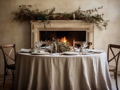 a table set with place settings and candles in front of a fire place that is lit