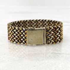 a gold and silver bracelet with a square clasp on the front, sitting on a white surface