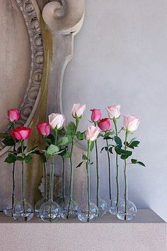 four vases with roses in them sitting on a shelf next to a mirror and clock