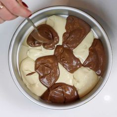 a bowl filled with chocolate and cream on top of a white counter next to a woman's hand