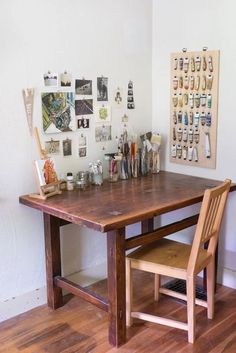 a wooden table sitting in front of a white wall with pictures on the wall behind it