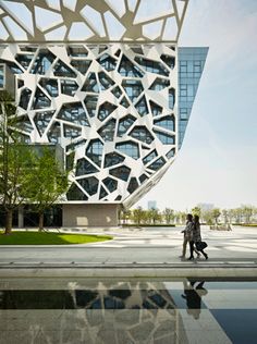 two people walking in front of a building with an unusual design on it's side