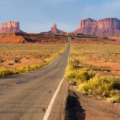 an empty road in the desert with mountains in the backgrouds and blue sky