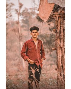 a young man standing next to a tree in the middle of a forest with no leaves on it