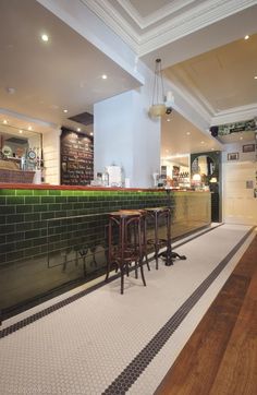 two wooden stools sitting in front of a green tiled bar with black and white checkered flooring