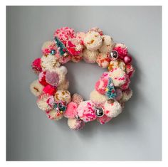 a wreath made out of teddy bears with pink and white flowers on it, sitting against a gray wall