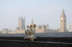 there is a small toy rabbit sitting on the ledge next to a building with big ben in the background